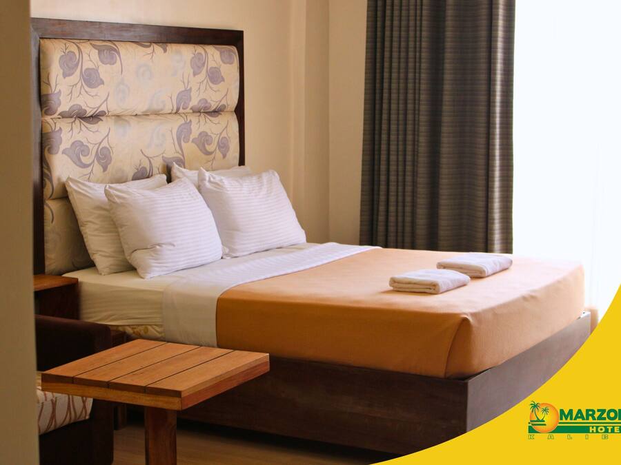 A hotel room with a bed, pillows, a wooden nightstand, and a table.