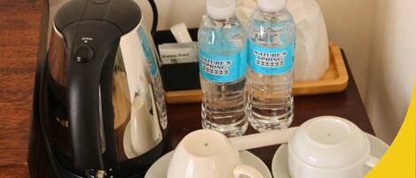 A hotel room with a coffee maker, two bottles of water, and tea sets on a wooden table.