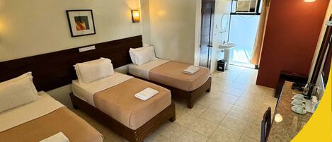 A hotel room with three beds, a bathroom with a sink and mirror, and a view of the outside.