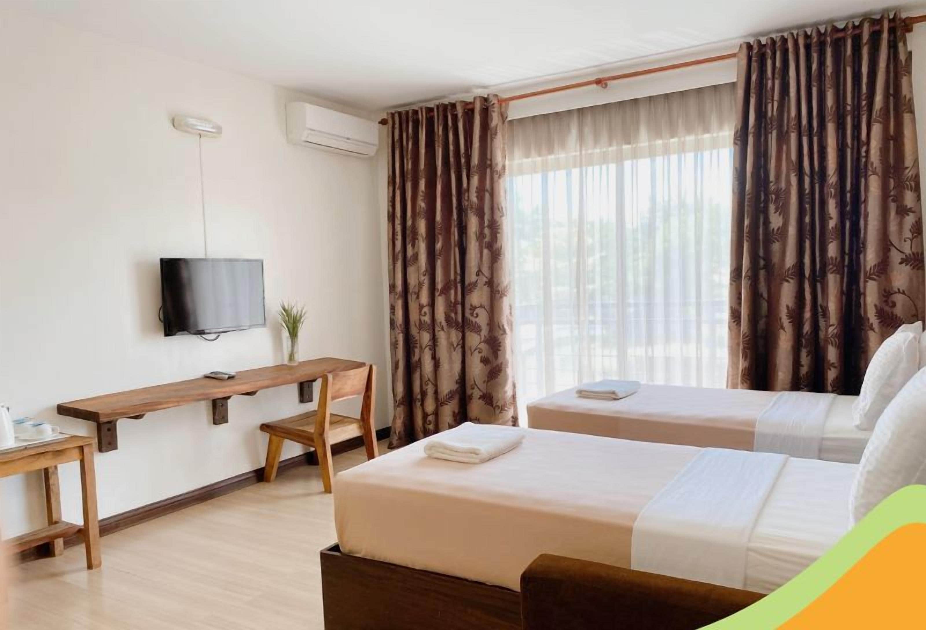 A hotel room with two beds, a desk, a TV, and a window with curtains.