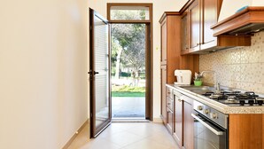 A kitchen with wooden cabinets, a gas stove, and a view through an open door to a backyard. - Pet-Friendly Apartment "Casa Museddu" with A/C, Terraces & Garden (Cardedu)
