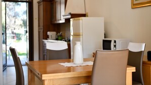 A dining area with a wooden table, chairs, a white vase, and a kitchen in the background. - Pet-Friendly Apartment "Casa Museddu" with A/C, Terraces & Garden (Cardedu)