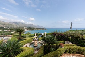A landscaped garden with a fountain, palm trees, and a view of the sea.