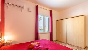 A bedroom with a bed, a wardrobe, a window with curtains, an air conditioning unit, and a bedside lamp. - Apartment 'Casa Rossa' with Sea View, Veranda & Wi-Fi (Castellammare del Golfio)