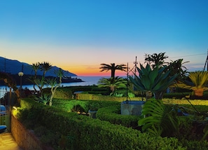 Un jardin aménagé offrant une vue sur la mer et les montagnes au coucher du soleil.