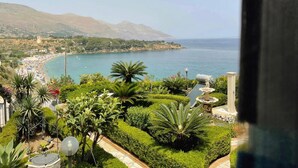 A coastal view with a beach, mountains, and a well-maintained garden with a fountain. - Apartment 'Casa Rossa' with Sea View, Veranda & Wi-Fi (Castellammare del Golfio)