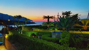 A landscaped garden with a view of the sea and mountains at sunset.