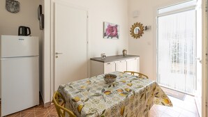 A compact kitchen with a refrigerator, a dining table with a patterned tablecloth, and a small cabinet.