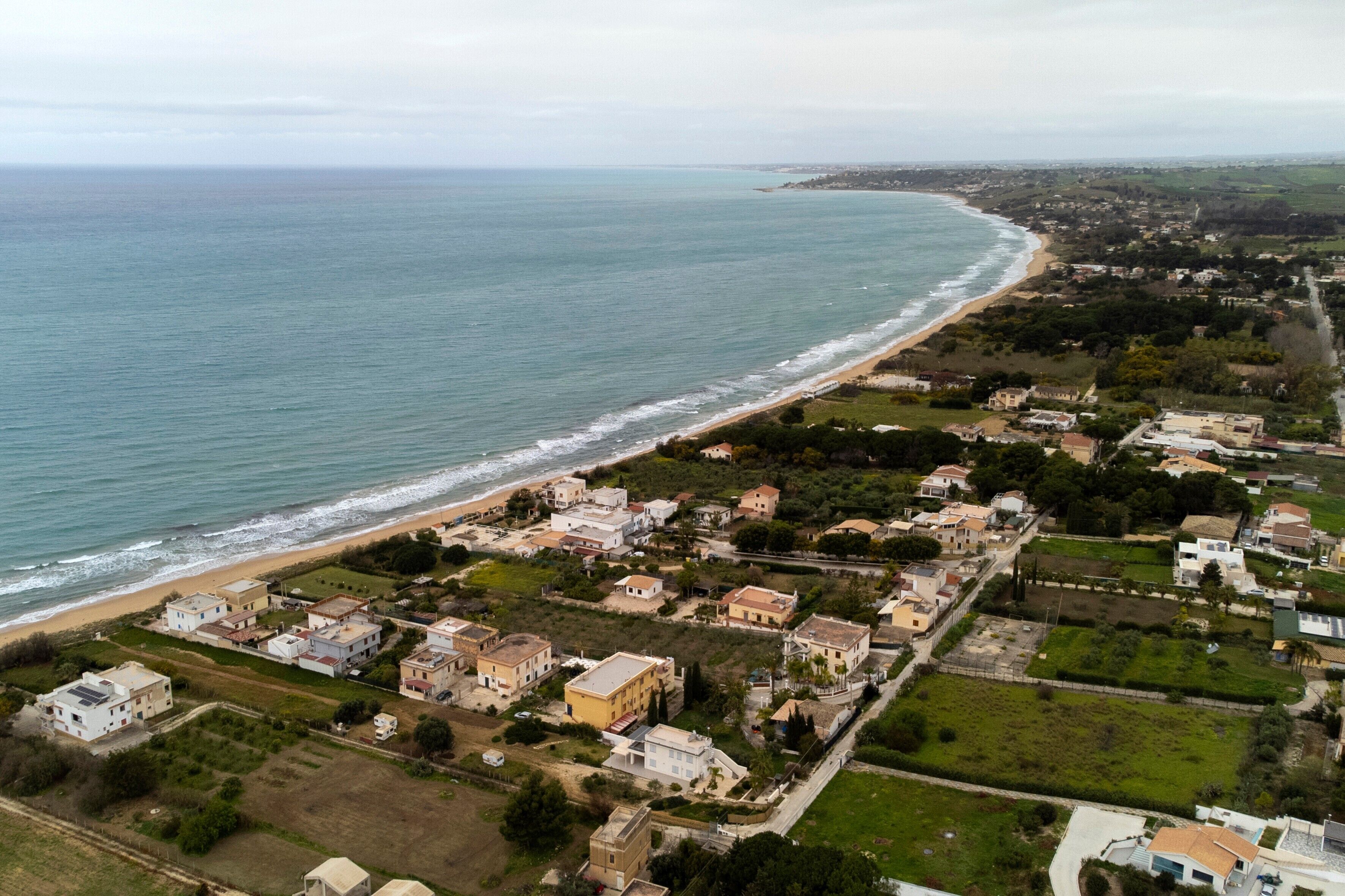 An aerial view of a coastal town with houses, a beach, and a road leading to the sea.