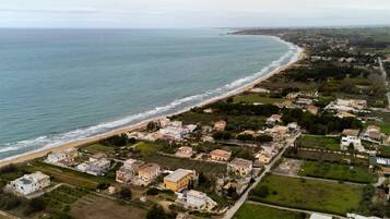 An aerial view of a coastal town with houses, a beach, and a road leading to the sea.