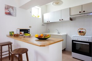 Una cocina con armarios blancos, una encimera de madera, un microondas, un fregadero y un horno.