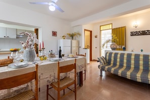 A dining area with a table set for four, a sofa, and a kitchen in the background.