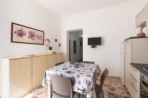 Un comedor con una mesa dispuesta para dos personas, un armario, un televisor y una zona de cocina.