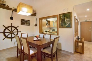 Un comedor con una mesa de madera, sillas, un adorno con timón de barco, un modelo de barco y un cuadro enmarcado.