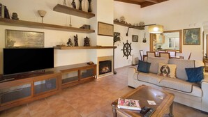 Ein Wohnzimmer mit Kamin, Fernseher, Sofa und diversen dekorativen Gegenständen auf Regalen.