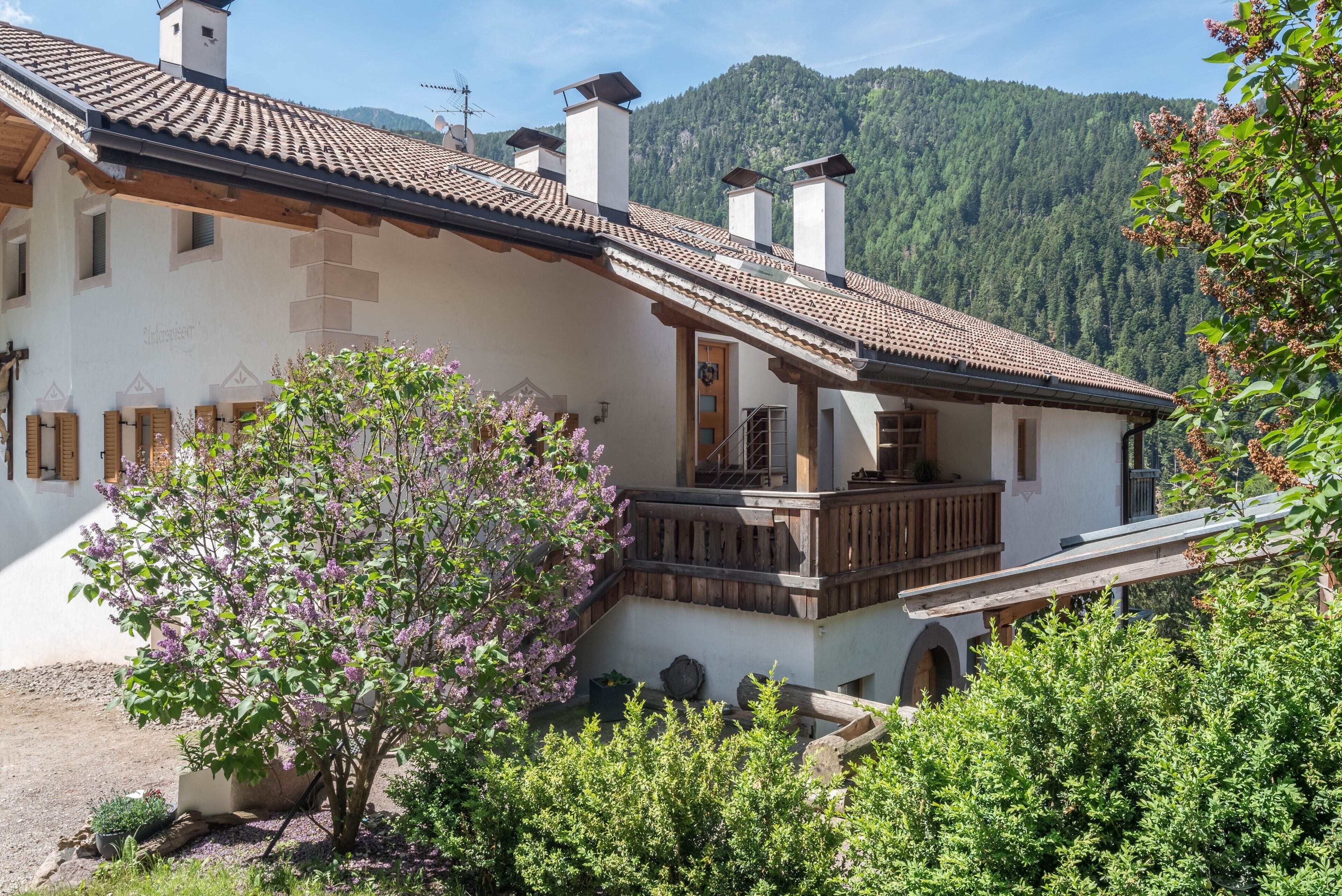 A traditional chalet with a balcony, wooden shutters, and a mountain backdrop.
