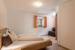 Un lit simple avec une tête de lit en bois, une table de chevet avec une lampe et une fenêtre avec des rideaux.
