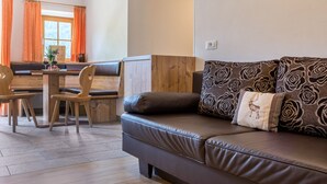 A modern living room with a brown leather sofa, wooden chairs, a dining table, and orange curtains. - Holiday Apartment "Ringelblume Biohof Unterspisser" with Mountain View, Balcony & Wi-Fi (Lajen)