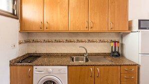 Una cocina con armarios de madera, lavadora integrada, microondas y un lavabo.