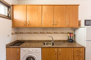 Une cuisine avec des meubles de rangement en bois, un lave-linge encastré, un four à micro-ondes et un évier.
