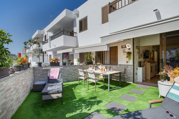 A modern apartment with a balcony, a dining area with a table and chairs, and a small kitchen visible through an open door.