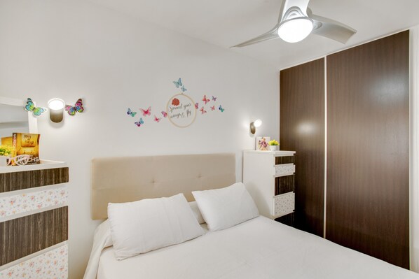 A bedroom with a bed, a nightstand, a dresser, a ceiling fan, and wall decorations.