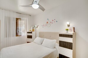 A bedroom with a bed, a ceiling fan, a nightstand, a wall-mounted light, and a decorative wall piece.