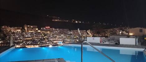 A rooftop pool with a view of a cityscape at night.