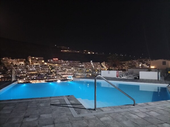 A rooftop pool with a view of a cityscape at night.