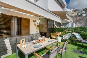 An outdoor dining area with a table set for two, surrounded by greenery and a view of a hillside.