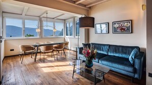 A spacious living area with a dining table, chairs, a sofa, and a coffee table. There are large windows providing a view of the mountains. - Apartment 'Kraidlhof - Designapartment Isabel' with Mountain View, Shared Pool & Wi-Fi (Kurtatsch)