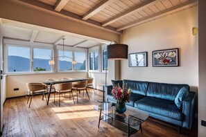 Un vaste espace de vie comprenant une table à manger, des chaises, un canapé et une table basse. De grandes fenêtres offrent une vue sur les montagnes.