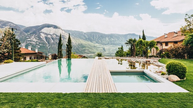 A swimming pool with a wooden deck, surrounded by well-maintained grass and trees, with mountains in the background. - Apartment 'Kraidlhof - Designapartment Isabel' with Mountain View, Shared Pool & Wi-Fi (Kurtatsch)