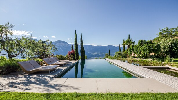A pool with lounge chairs, surrounded by greenery and mountains in the background. - Apartment "Kraidlhof Designapartment Veronika" with Mountain View, Shared Pool and Wi-Fi (Kurtatsch)