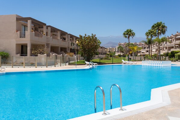 A swimming pool with lounge chairs, a building with balconies, and palm trees.