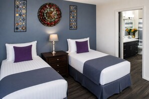 Ein Hotelzimmer mit zwei Betten, einem Nachttisch mit Lampe, Wanddekoration und Blick ins Badezimmer durch eine geöffnete Tür.