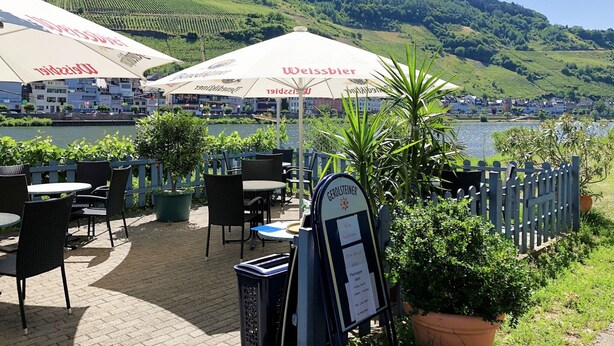 An outdoor seating area with tables and chairs, umbrellas, and a signboard.