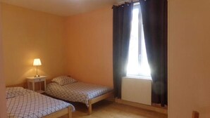 A room with two wooden beds, a bedside table with a lamp, a window with curtains, and a radiator.