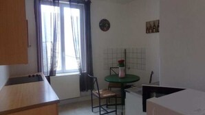 A small kitchen with a window, a dining table with chairs, and a refrigerator.