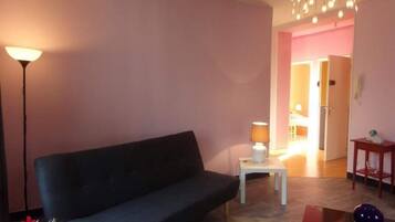 A living room with a dark sofa, a small white table with a lamp, and a decorative vase.