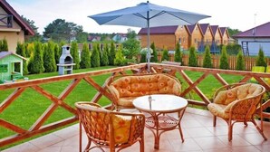 An outdoor patio with wicker furniture, a round table, and a large umbrella. - Half of holiday home, terrace, playground (Rowy)