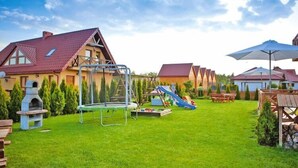 A residential area with a grassy yard, a trampoline, a slide, and a barbecue grill. - Half of holiday home, terrace, playground (Rowy)