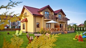 A two-story house with a balcony, a lawn, and outdoor furniture. - Half of holiday home, terrace, playground (Rowy)