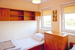 A small, single-bed room with a wooden dresser, a window with a view, and a shelf above the bed. - Half of holiday home, terrace, playground (Rowy)