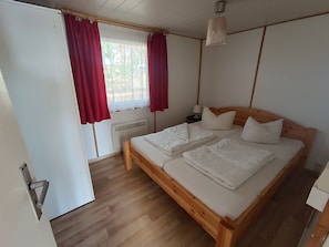 Una camera da letto con un letto in legno, biancheria bianca, un comodino con una lampada e una finestra con tende rosse.