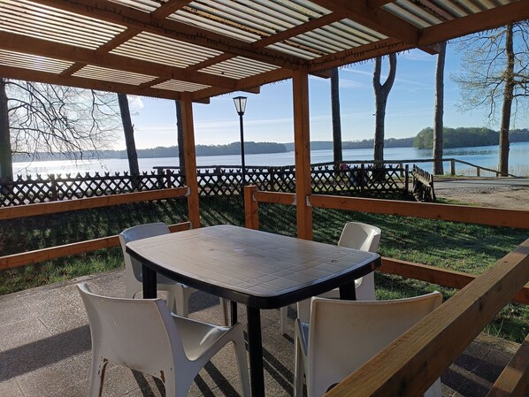 A covered outdoor seating area with a table and chairs, overlooking a lake.