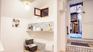 Een badkamer met douche, toilet en wastafel; een klein schapje met toiletartikelen; een spiegel aan de muur; en een deur die leidt naar een binnentuin.