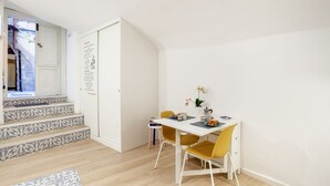 Een kamer met een witte deur, een trap met decoratieve treden, een eettafel met gele stoelen en een kleine potplant.