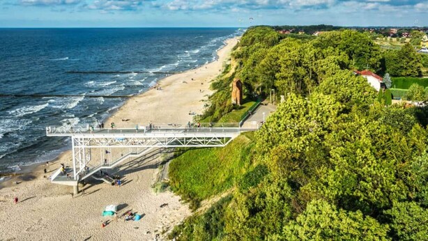 A beach with a pedestrian bridge, sandy shore, and lush greenery.