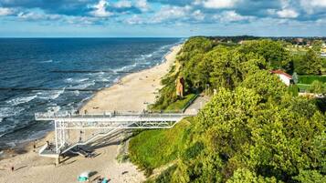 A beach with a pedestrian bridge, sandy shore, and lush greenery.